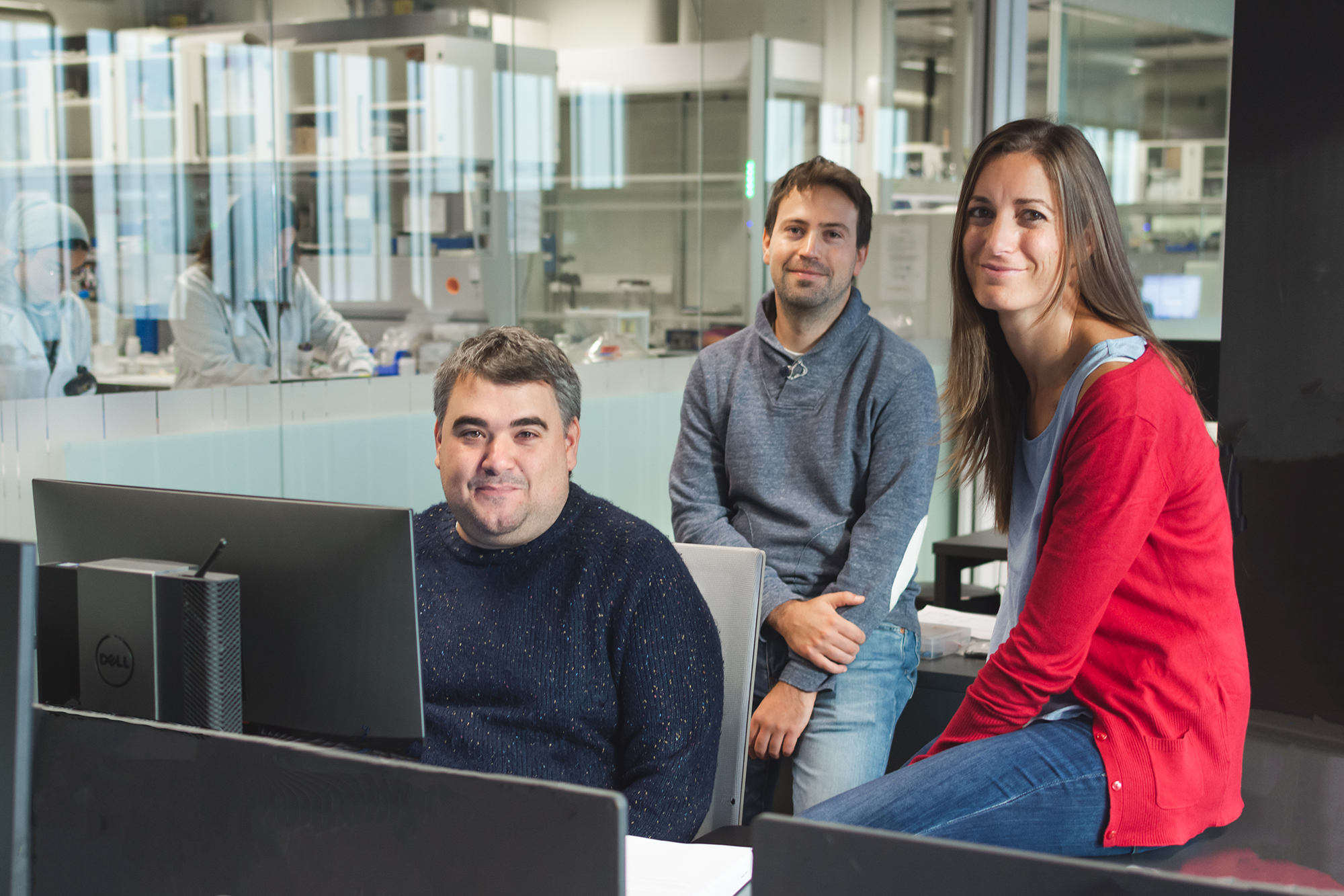 Three of CIC energiGUNE´s workers that take part in the PULSELiON project pose in a common working area in front of a laboratory, where it seems that there are researchers working.